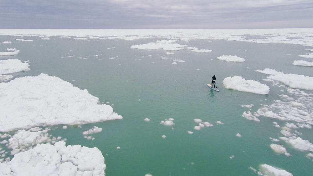 Surfing one week and riding his Stand-up paddleboard, Karol Garrison joins Lake Michigan ice in motion. Photo by Seth Haley/sethhaley.com.